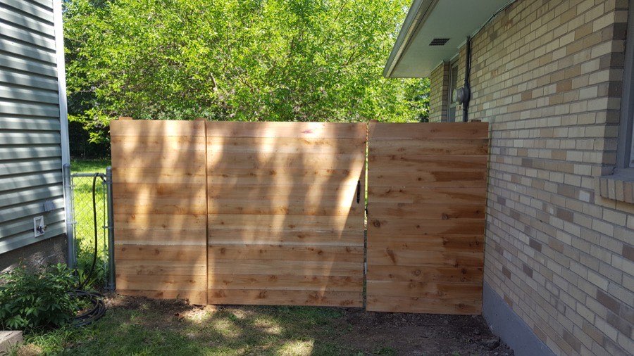 Horizontal cedar plank fence and gate beside a brick home